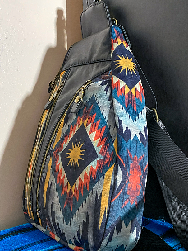Handmade crossbody bag with black leather and bronze accents, featuring a vibrant sun-inspired fabric design in yellow, red, and blue, adjustable crossbody strap, and eye-catching colorful interior