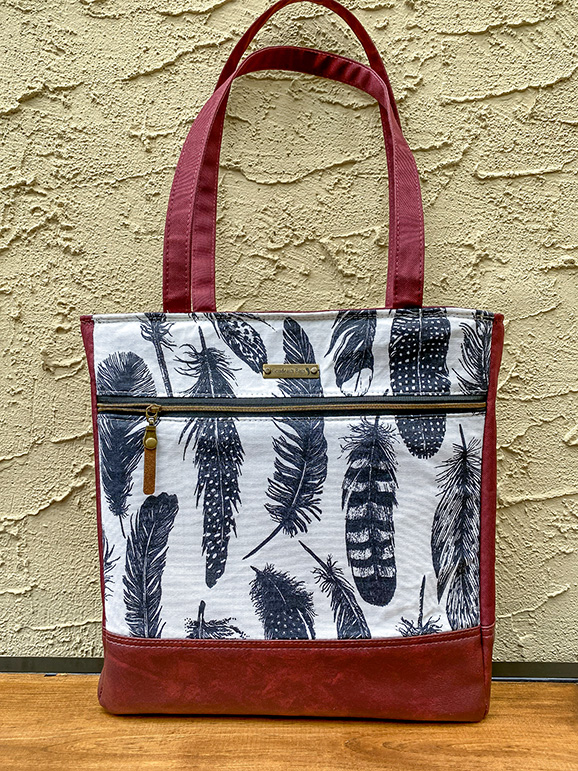 Handmade one-of-a-kind leather tote with feather print accents, carry handles, shoulder strap, standing feet, and functional interior pockets