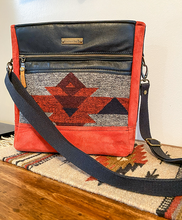 Handmade red tote featuring bright red faux suede, black faux leather, black carrying strap, and a red, black, and grey Native American–inspired pattern, designed for everyday use with quality materials