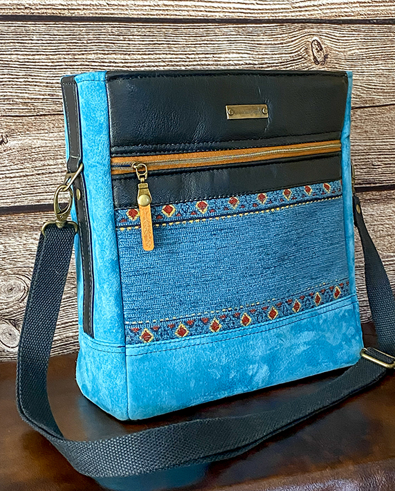 Handcrafted crossbody bag with Native American-inspired detailing, adjustable strap, and zippered storage pockets